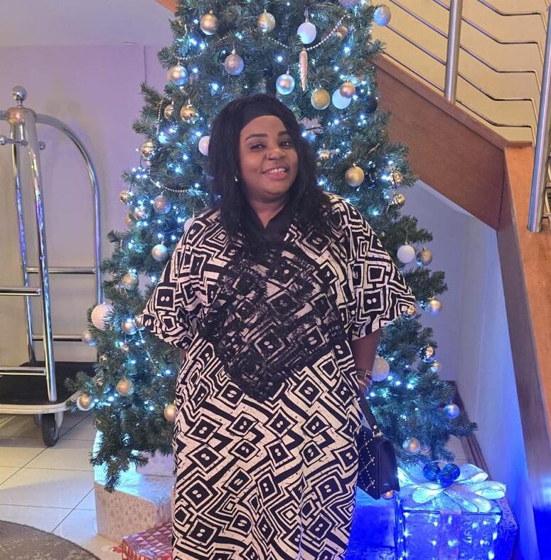Evelyn is stood in front of a christmas tree in a black and white African print dress
