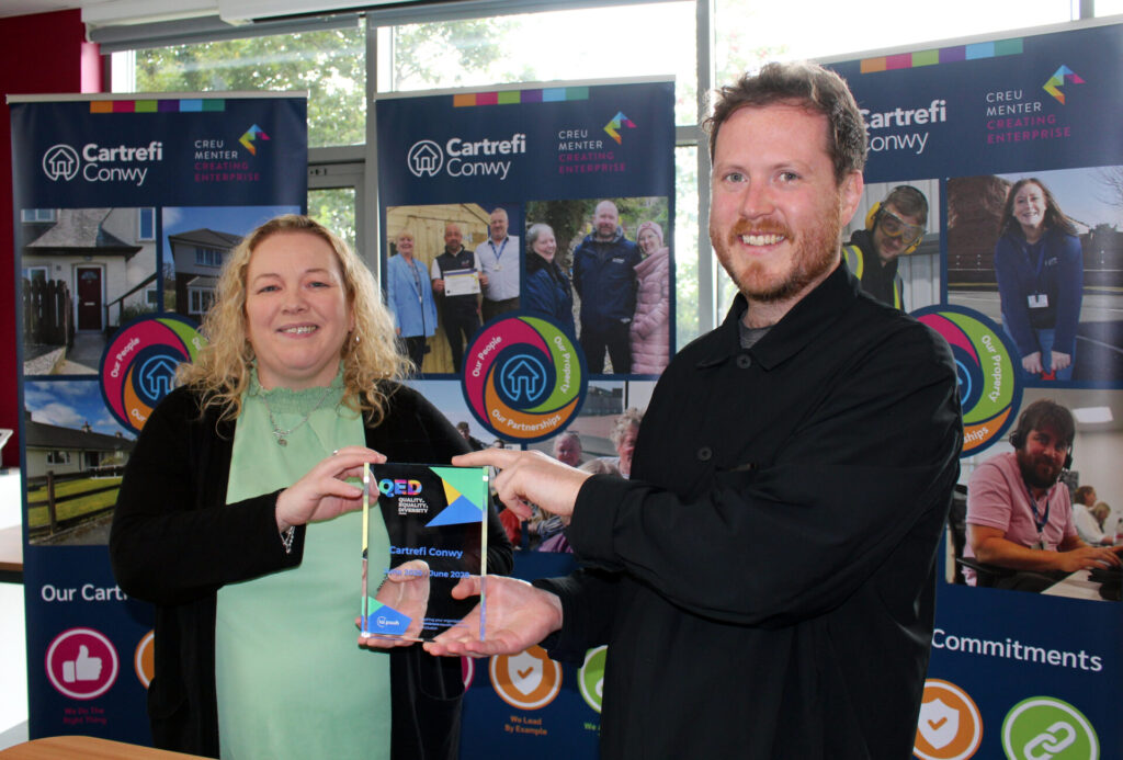 Rob Milligan, our Funding and Partnerships Manager, is handing our glass QED Award to Lesley Stones, Housing Management Lead at Cartrefi Conwy.